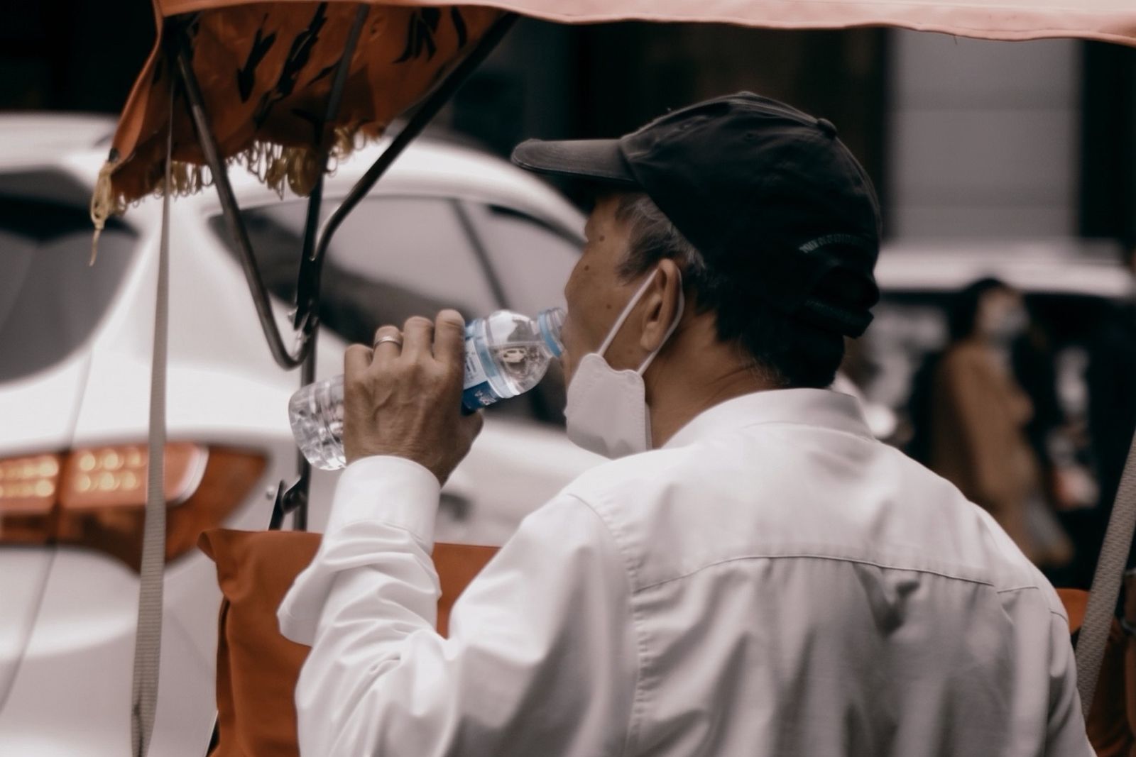 一位中年男子坐在三輪車上仰頭大口飲用瓶裝礦泉水的情境特寫,呈現日常生活中邊忙邊喝水、仰頭吞嚥容易引發喉嚨肌力不足嗆咳的危險習慣。 一位中年男子坐在三輪車上仰頭大口飲用瓶裝礦泉水的情境特寫,呈現日常生活中邊忙邊喝水、仰頭吞嚥容易引發喉嚨肌力不足嗆咳的危險習慣。